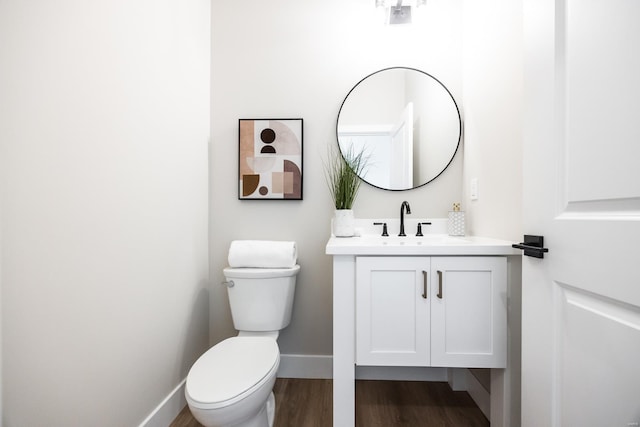 half bathroom with toilet, vanity, baseboards, and wood finished floors