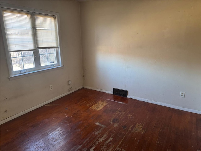 empty room featuring hardwood / wood-style floors, visible vents, and baseboards