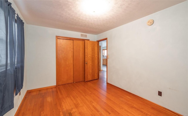 unfurnished bedroom with baseboards, visible vents, light wood-style flooring, a textured ceiling, and a closet