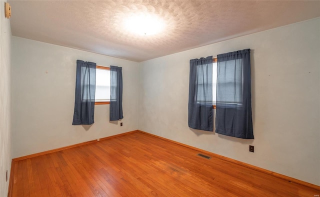 empty room featuring wood-type flooring, visible vents, a textured ceiling, and baseboards