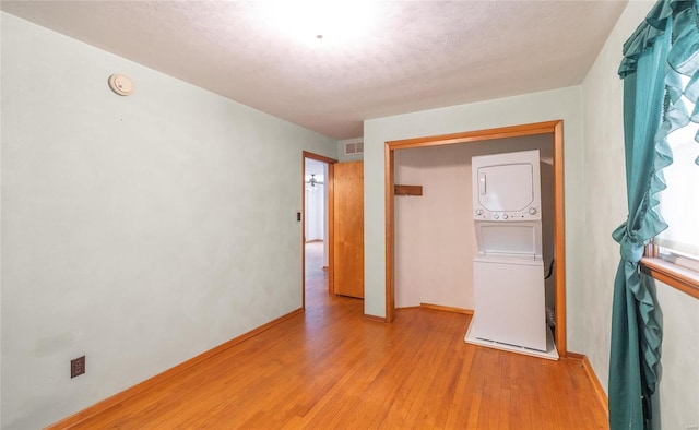 unfurnished bedroom featuring a textured ceiling, stacked washer and dryer, light wood-type flooring, and visible vents