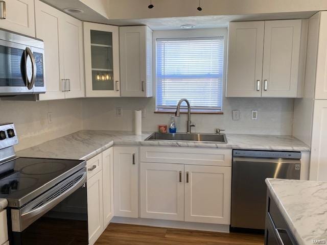 kitchen featuring appliances with stainless steel finishes, glass insert cabinets, white cabinets, a sink, and wood finished floors