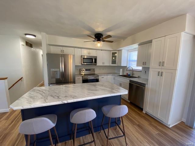 kitchen featuring a breakfast bar, visible vents, appliances with stainless steel finishes, white cabinetry, and a sink