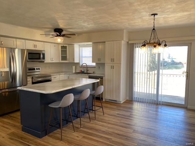 kitchen with white cabinets, wood finished floors, a center island, stainless steel appliances, and a kitchen bar