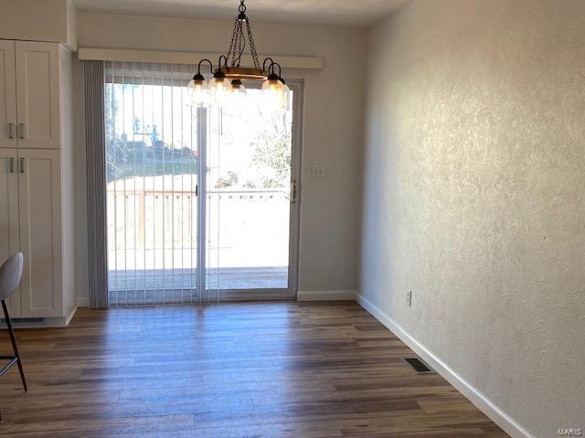 unfurnished dining area featuring a textured wall, visible vents, baseboards, dark wood finished floors, and an inviting chandelier