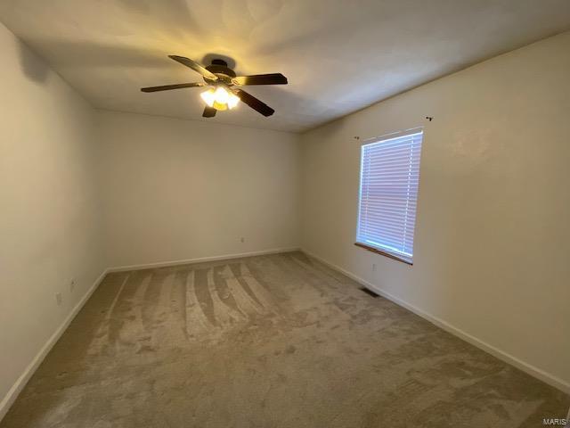 carpeted spare room featuring a ceiling fan, visible vents, and baseboards