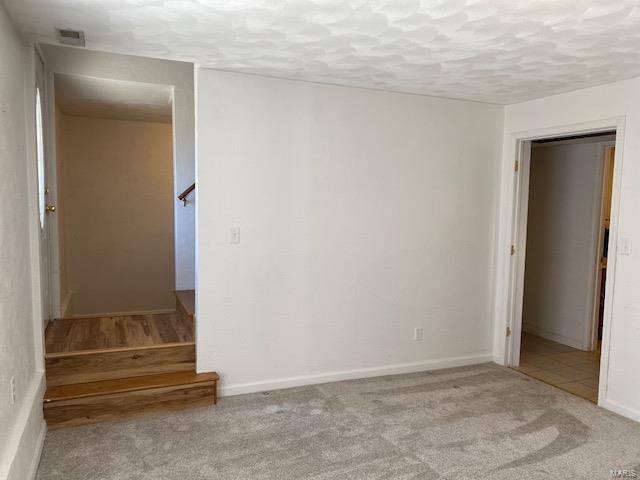 carpeted spare room with a textured ceiling, stairway, visible vents, and baseboards