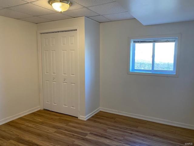 unfurnished bedroom featuring a closet, a drop ceiling, baseboards, and wood finished floors