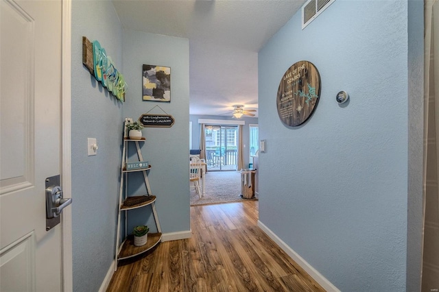 hallway featuring baseboards, visible vents, and wood finished floors