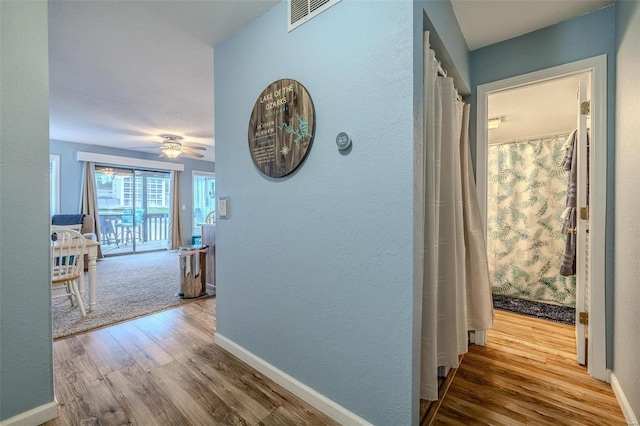 hallway with wood finished floors, visible vents, and baseboards