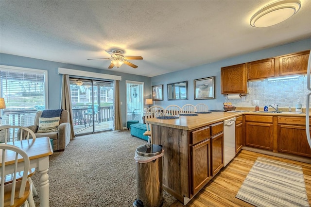 kitchen with brown cabinetry, a peninsula, white dishwasher, light countertops, and backsplash