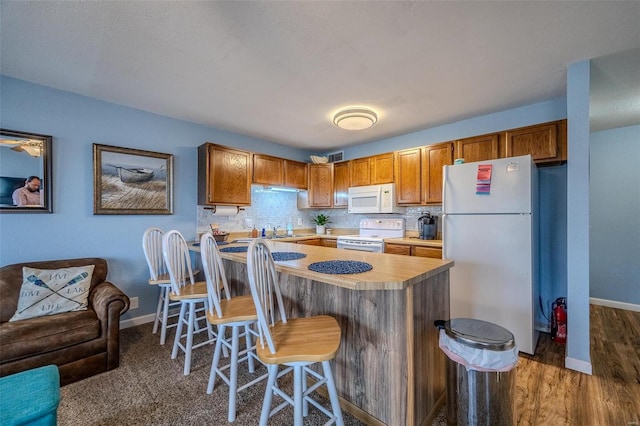 kitchen with a kitchen bar, backsplash, a sink, white appliances, and baseboards