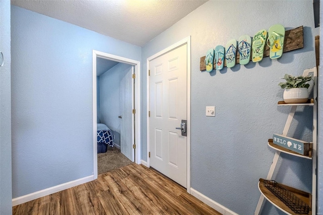 corridor featuring a textured wall, a textured ceiling, baseboards, and wood finished floors