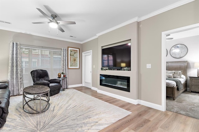 living area with light wood finished floors, visible vents, crown molding, and a glass covered fireplace