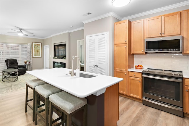 kitchen featuring stainless steel appliances, visible vents, ornamental molding, open floor plan, and a sink