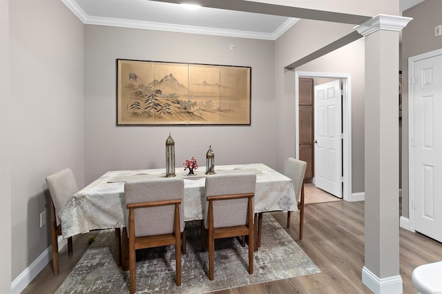 dining room featuring baseboards, crown molding, light wood finished floors, and ornate columns