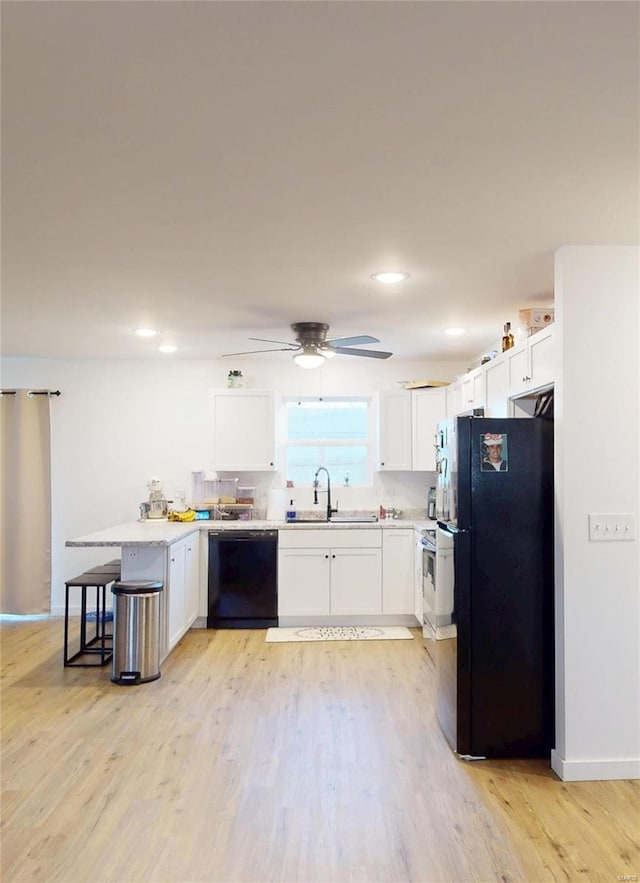 kitchen featuring black appliances, a peninsula, light wood-style floors, white cabinetry, and a sink