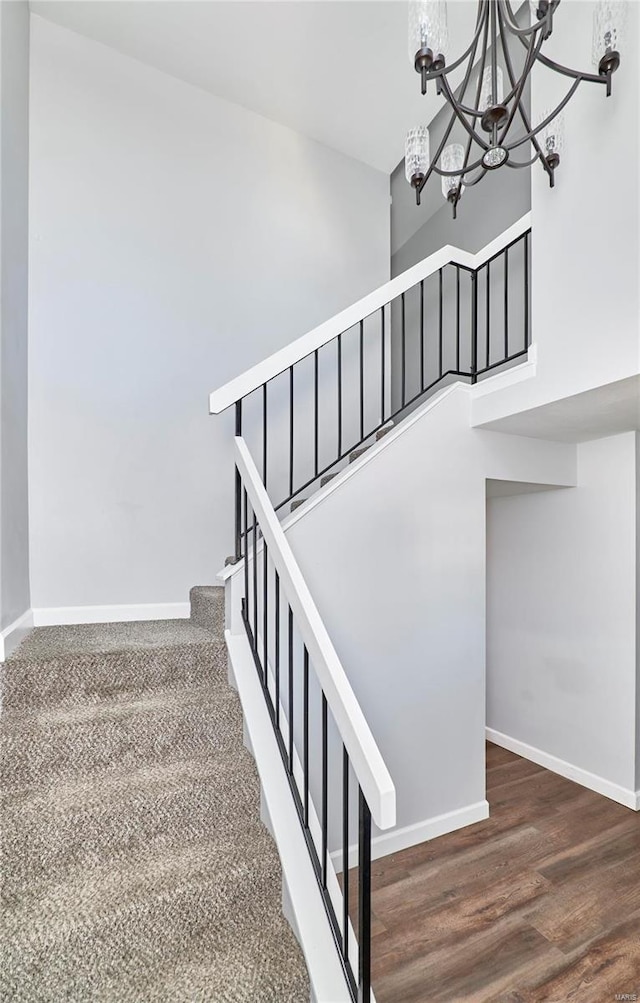 stairs featuring a chandelier, a towering ceiling, baseboards, and wood finished floors