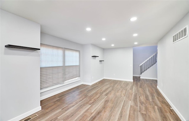 unfurnished living room featuring recessed lighting, wood finished floors, visible vents, baseboards, and stairway