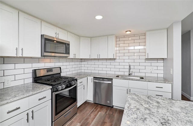 kitchen with appliances with stainless steel finishes, dark wood-style flooring, a sink, and light stone counters