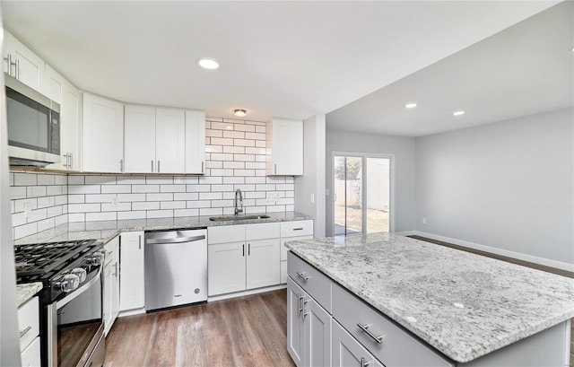 kitchen with light stone counters, stainless steel appliances, dark wood-style flooring, a sink, and decorative backsplash