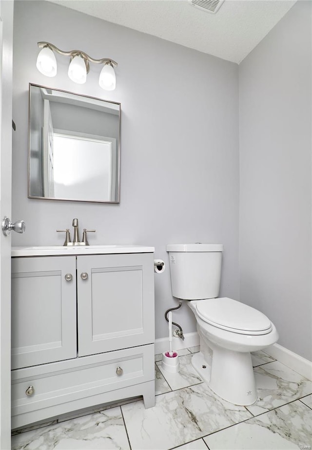 bathroom featuring toilet, visible vents, vanity, baseboards, and marble finish floor