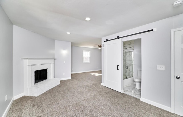 unfurnished living room featuring a barn door, recessed lighting, a fireplace, baseboards, and carpet