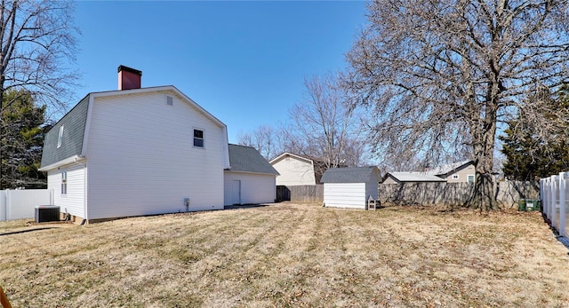 rear view of house featuring a fenced backyard, a shed, cooling unit, and an outbuilding