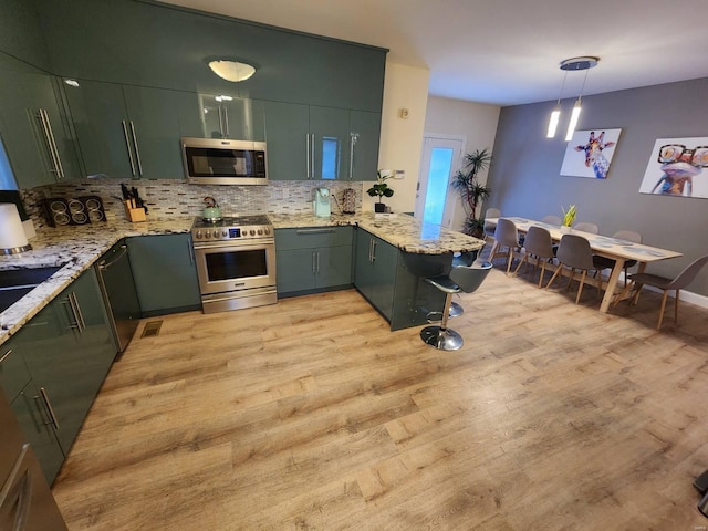 kitchen featuring a peninsula, light wood-style floors, appliances with stainless steel finishes, and decorative backsplash