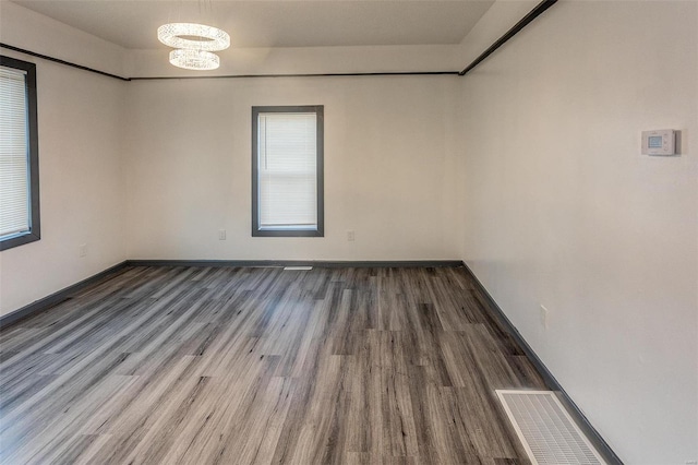 spare room with a chandelier, visible vents, baseboards, and wood finished floors