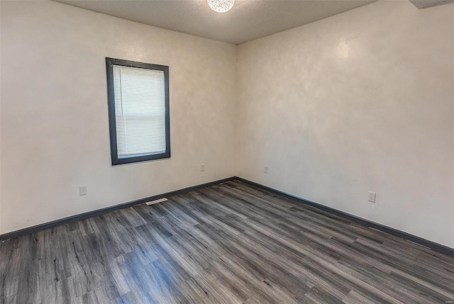 empty room featuring baseboards and dark wood-type flooring