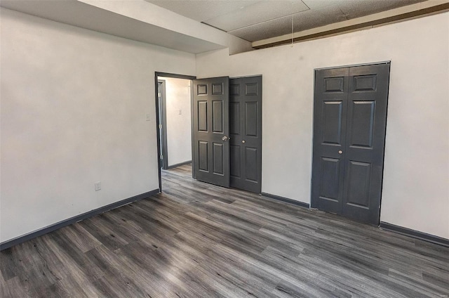 unfurnished bedroom featuring attic access, dark wood-style flooring, a closet, and baseboards