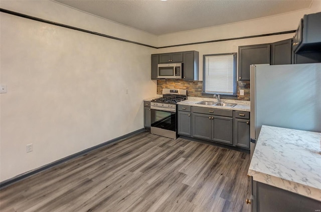 kitchen with stainless steel appliances, dark wood-type flooring, a sink, light countertops, and decorative backsplash