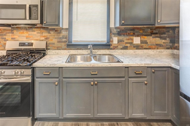 kitchen with appliances with stainless steel finishes, a sink, gray cabinetry, and tasteful backsplash