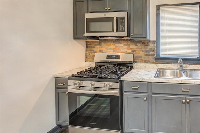 kitchen featuring stainless steel appliances, tasteful backsplash, a sink, and gray cabinetry