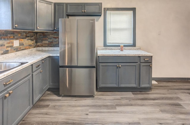 kitchen featuring light wood finished floors, gray cabinets, backsplash, and freestanding refrigerator