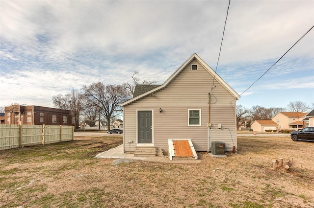 rear view of property featuring entry steps, central air condition unit, fence, and a lawn