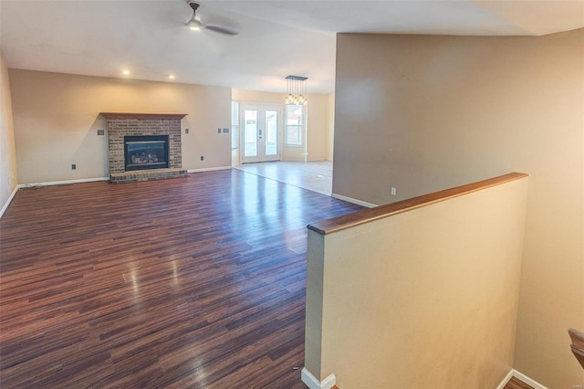 unfurnished living room featuring dark wood-style floors, french doors, a fireplace, a ceiling fan, and baseboards