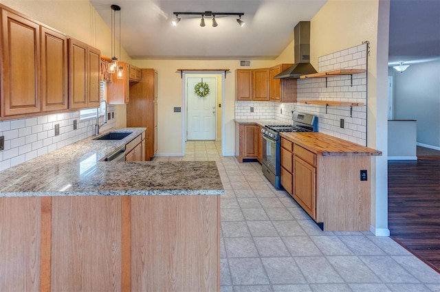 kitchen with open shelves, stainless steel range with gas stovetop, a sink, wall chimney range hood, and light stone countertops