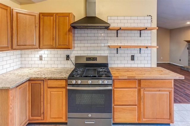 kitchen featuring stainless steel gas range oven, butcher block countertops, wall chimney range hood, backsplash, and open shelves