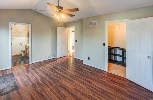 unfurnished bedroom with dark wood-style flooring, lofted ceiling, visible vents, ensuite bathroom, and baseboards