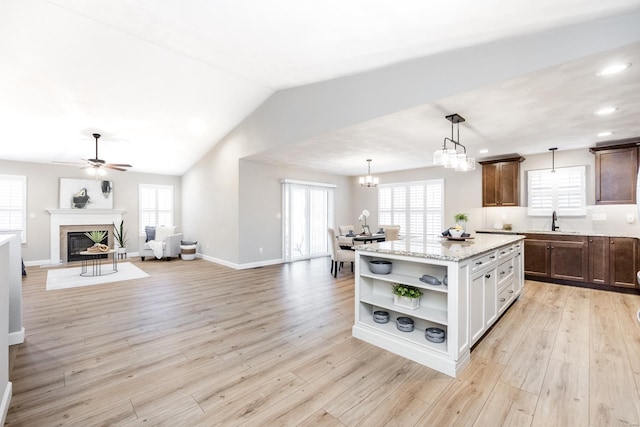 kitchen featuring vaulted ceiling, a fireplace with flush hearth, light wood-style floors, and open shelves