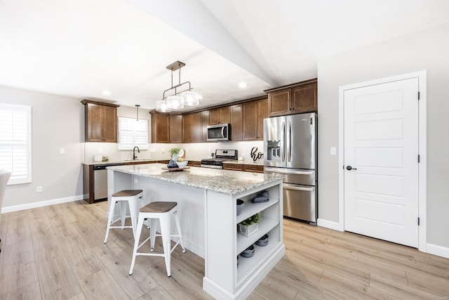 kitchen featuring open shelves, a kitchen island, appliances with stainless steel finishes, light wood-style floors, and a sink