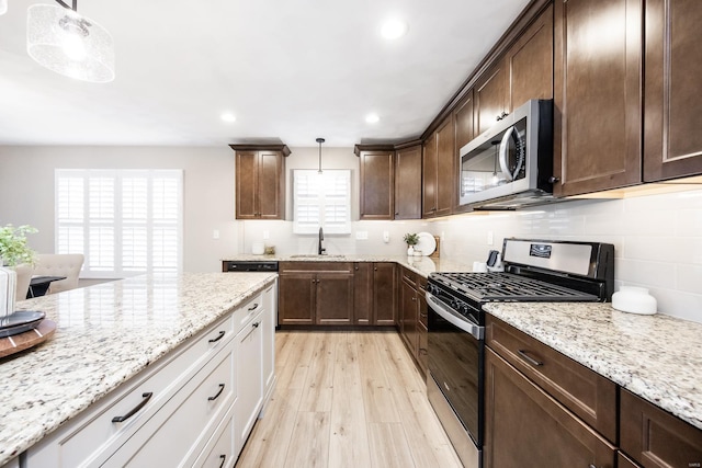 kitchen featuring tasteful backsplash, dark brown cabinets, appliances with stainless steel finishes, light wood-style floors, and a sink