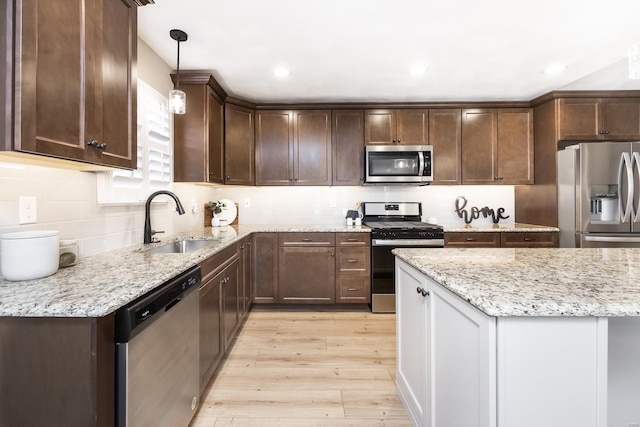 kitchen with light wood finished floors, a sink, stainless steel appliances, dark brown cabinetry, and backsplash