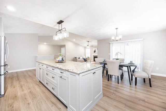 kitchen featuring light wood-style flooring, a kitchen island, a fireplace, vaulted ceiling, and hanging light fixtures