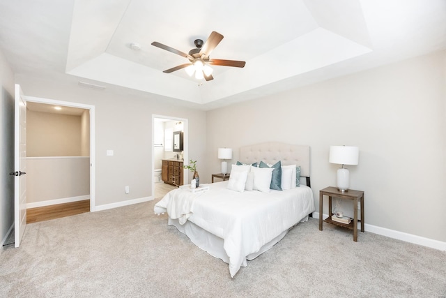 bedroom with baseboards, a raised ceiling, light carpet, and connected bathroom