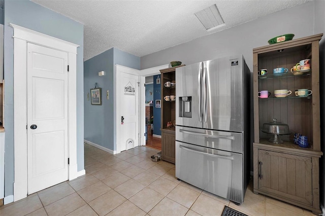 kitchen with a textured ceiling, open shelves, light tile patterned flooring, and stainless steel fridge