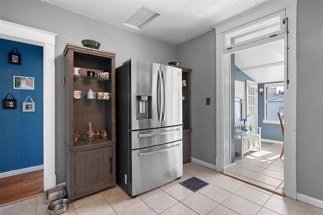 kitchen featuring light tile patterned floors, visible vents, a textured ceiling, and stainless steel fridge with ice dispenser