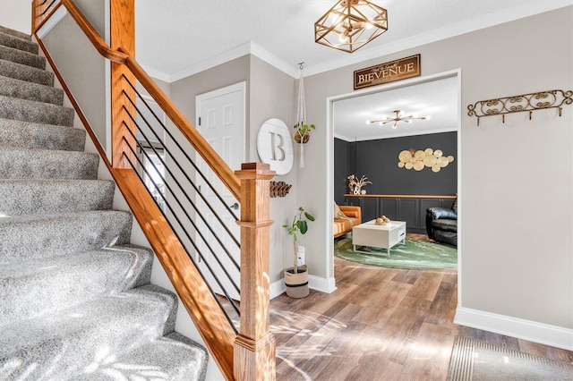 staircase with a textured ceiling, wood finished floors, baseboards, and ornamental molding